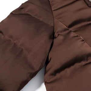Gros plan des coutures et du tissu brillant marron foncé de la veste matelassée
