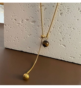 Gros plan sur une perle oeil de tigre et chaîne serpent dorée sur une pierre texturée