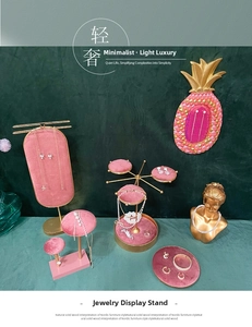 Pink velvet jewelry display set with gold metal bases on dark green backdrop