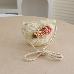 Detail of a beige straw crossbody bag featuring lace trim and two handmade floral accents