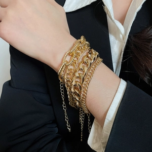 Detail showing layered gold metal chain bracelets with various link styles on wrist