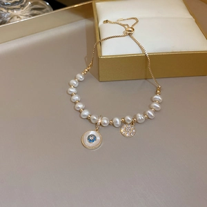 Detailed view of gold pearl bracelet with floral charm and adjustable sliding clasp