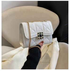 Detailed view of white quilted crossbody bag with heart pattern and gold chain