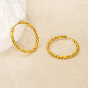 Elegant gold twisted rope hoop earrings displayed on a minimalist white stone background