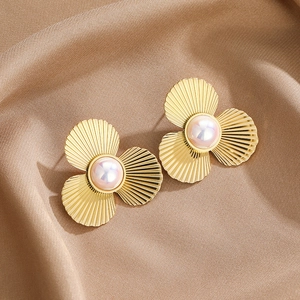 Golden three-petal flower stud earrings with soft pink pearls on elegant silk fabric