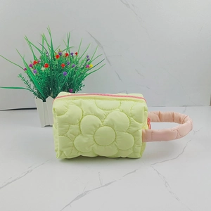 Detail of yellow quilted makeup bag with 3D floral texture and pink handle