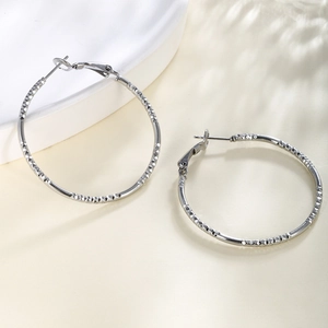 Detail of silver hoop earrings featuring textured diamond-cut pattern and pin closure