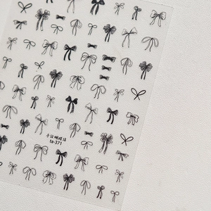 Macro view of hand-drawn black bow nail decals with fine line details on a white background