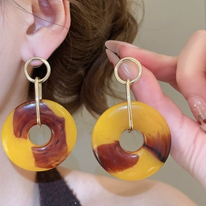 Close-up of geometric resin teardrop earrings in amber yellow with gold metal detail
