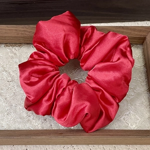 Detail of red satin oversized scrunchie showing glossy silk texture on a glass tray