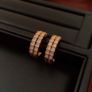 Macro shot of gold-plated snake-scale earrings featuring rectangular crystals on black leather