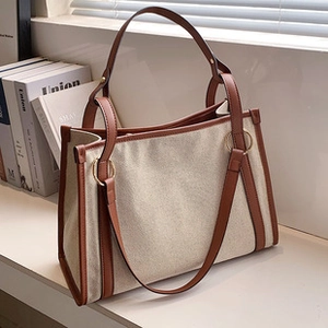 Detailed view of the beige canvas tote bag with brown leather trim and metal ring hardware