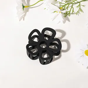 Detail of a matte black flower hair claw clip with a hollow six-petal design on white surface