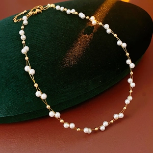 Detail of a double-layered white pearl necklace with gold beads on green velvet