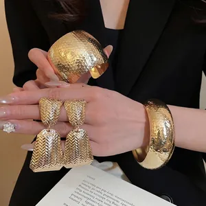 Textured gold bangle set and matching geometric earrings on a professional model