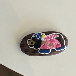 Macro detail of a hand-knitted hair clip featuring a cute puppy embroidery and Happy text