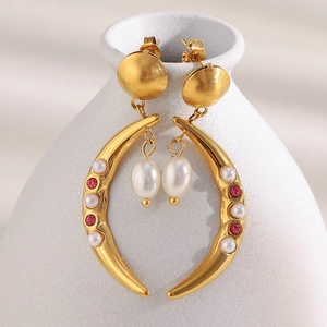 18K gold plated horn earrings with white pearls and red gemstones on ceramic surface