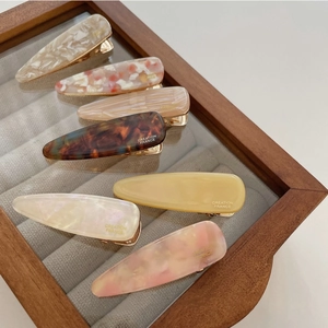 Set of seven marble and pearl acetate hair clips displayed in a wooden jewelry tray