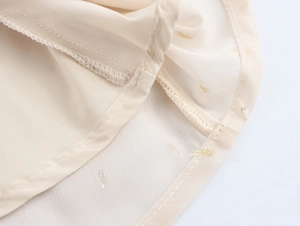 Macro shot of apricot chiffon fabric with gold jacquard dots and hem sewing details