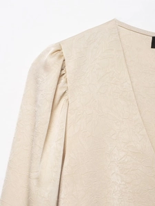 Détail du chemisier plissé champagne montrant le col en V et la texture satinée