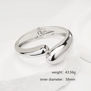 Close-up of minimalist silver irregular open bangle on a white textured stone base