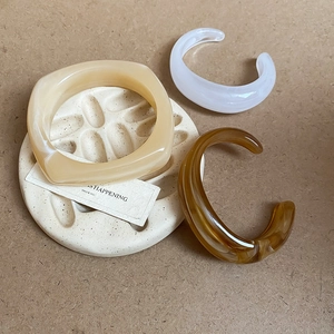 Three acrylic bangles in cream, white, and amber brown on a ceramic display tray
