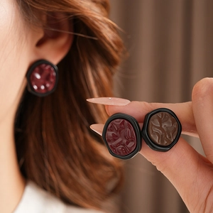 Detail of model wearing irregular geometric earrings in deep red and brown textured resin