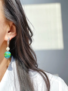 Detail of silver earring with white pearl and patterned green glass bead on a model