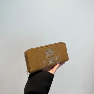 Hand holding a camel suede long wallet featuring a sparkling rhinestone skull and crossbones