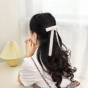 Detail of elegant white handmade pearl bow hair clip with long tassel on woman's hairstyle