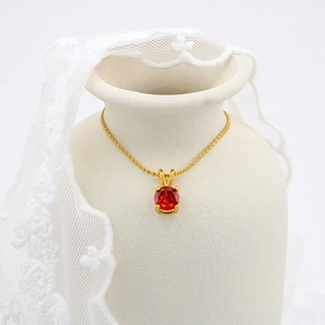 Detail shot of a red gemstone pendant on a gold chain draped over a ceramic vase