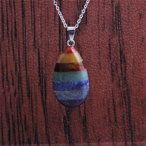 Detailed view of teardrop chakra pendant with colorful natural stones on wood surface