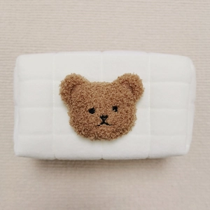 Detailed macro view of white quilted plush pouch featuring embroidered brown bear design