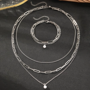 Macro detail of silver layered chain necklace set with white pearl pendants on black background