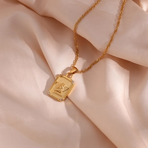Detailed close-up of golden rectangular angel pendant necklace on silk fabric