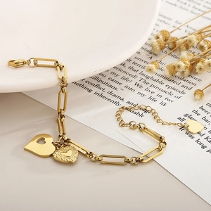 Detail of golden heart charms on paperclip link bracelet over a decorative ceramic plate