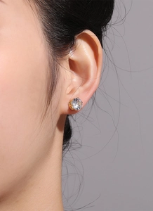 Gros plan d'une boucle d'oreille couronne dorée avec zircone portée sur l'oreille