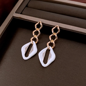 Detailed macro view of gold geometric earrings featuring white enamel and crystal stones