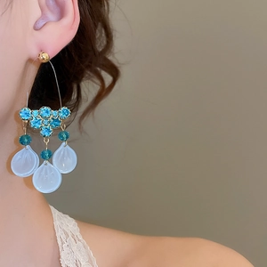 Close-up of elegant gold drop earrings with blue crystals and white frosted petal charms