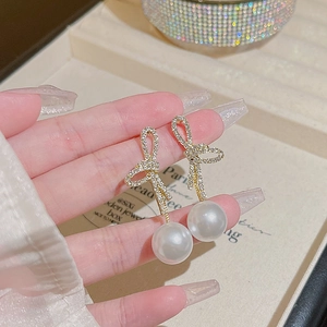 Close-up of golden bow-shaped earring with diamonds and a large drop pearl charm