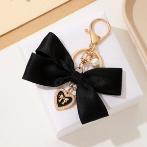 Detailed shot of black satin bow keychain with gold heart charm and pearl on a gift box