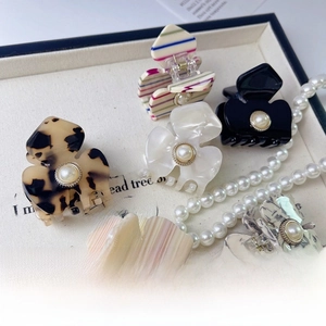 Close-up of floral acetate hair claws with pearls on a decorative vintage fabric tray
