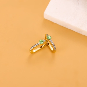 Detail of gold earrings featuring a green round stone and white zircon accents