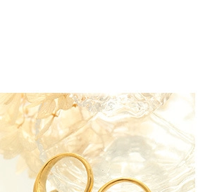 Close-up of a hollow C-shaped gold earring displayed on a textured glass surface