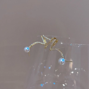 Detailed view of wave-shaped gold pearl earrings with crystal inlay on a glass rim