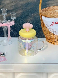 Iridescent glass cup with rainbow dots, cloud handle, yellow lid and straw in outdoor setting