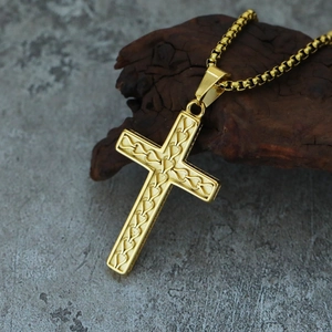 Macro shot of gold cross pendant with intricate textures on a grey marble surface