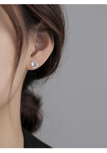 Macro shot of a silver Saturn stud earring with blue glass stone and zircon on a model