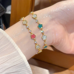 Detailansicht der goldenen Kleeblatt-Armbänder mit Zirkonia und Emaille am Handgelenk