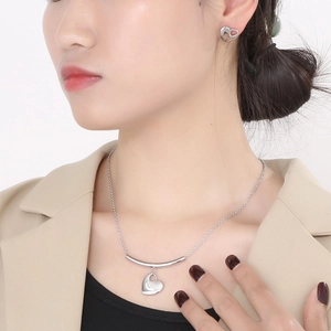 Close-up of silver stainless steel heart necklace and stud earrings set on a model